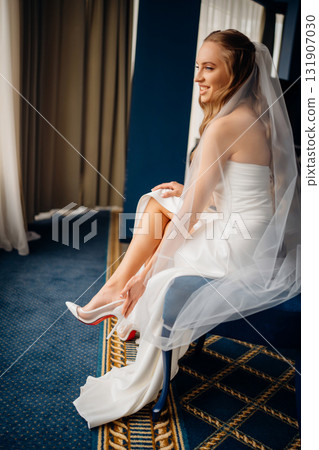 The bride in simple beautiful elegant wedding dress puts on shoes The bride in simple beautiful elegant wedding dress puts on shoes 131907030