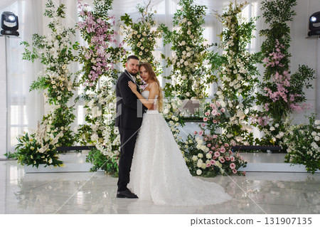 The bride and groom in front of the table in banquet hall decorated with flowers 131907135
