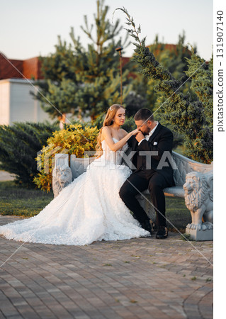 Gentle and happy bride and groom at sunset in the park on a bench. Gentle and happy bride and groom at sunset in the park on a bench. 131907140