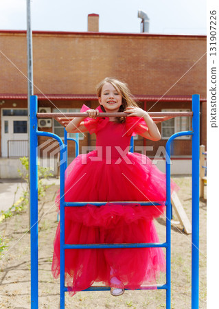 A cute little girl in an elegant lush pink dress is playing on the sports ground A cute little girl in an elegant lush pink dress is playing on the sports ground 131907226