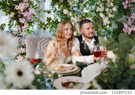 The bride and groom at the newlyweds' table, decorated with many flowers.  131907232