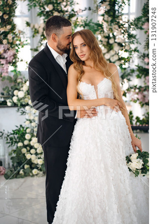 The bride and groom embrace affectionately in a room decorated with many flowers 131907248