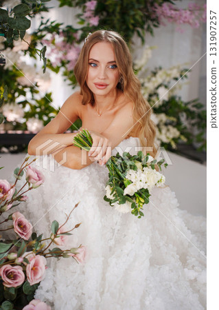 Beautiful bride with long blonde hair sitting surrounded by flowers.  131907257