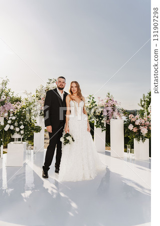The bride and groom at the wedding ceremony site, decorated with flowers The bride and groom at the wedding ceremony site, decorated with flowers 131907298