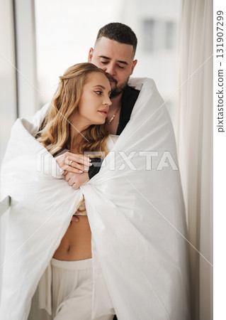 A gentle and romantic man and woman wrapped in a blanket on the windowsill A gentle and romantic man and woman wrapped in a blanket on the windowsill 131907299