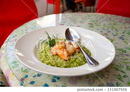 spinach risotto with shrimp and scallops on a white plate in a cozy Italian restaurant 131907956