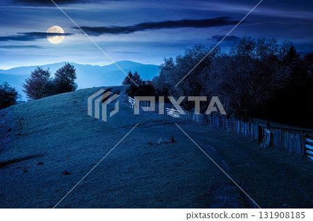 mountainous rural landscape in autumn at night. field behind the wooden fence in full moon light. scenery in fall season. forest on the hill. ridge in the distance 131908185