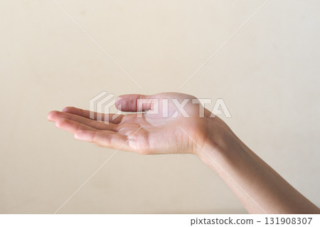 A close-up of a human hand with an open palm, resting against a plain beige background. The hand appears to be of a young adult with light skin. 131908307