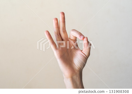 A close-up of a human hand making an 'OK' gesture against a neutral background. Gyan mudra. The hand is of a young adult with light skin and slender fingers. 131908308