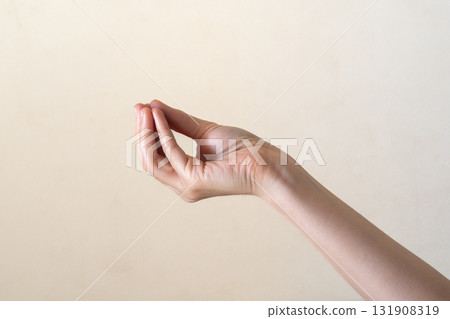 A close-up of a human hand making a gesture with fingers positioned in a pinching manner. The background is a soft, neutral color. 131908319
