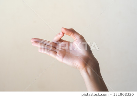 A close-up of a human hand making an 'OK' gesture against a neutral background. Gyan mudra. The hand is of a young adult with light skin and slender fingers. 131908320
