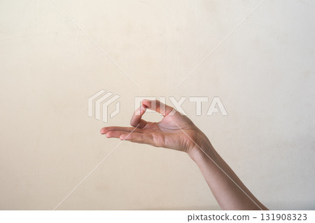 A close-up of a human hand making an 'OK' gesture against a neutral background. Gyan mudra. The hand is of a young adult with light skin and slender fingers. 131908323