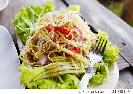 Thai spicy mango salad with crispy fish and vegetable in white dish on wooden table 131908369