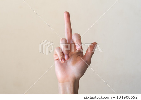 A close-up of a human hand showing a raised middle finger. The hand is pale with well-groomed nails. The background is a neutral color, creating a simple composition. 131908552