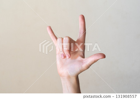 A close-up of a human hand making the 'I love you' sign in American Sign Language. The background is a neutral color, emphasizing the hand gesture. A close-up of a human hand making the 'I love you' sign in American Sign Language. The background is a neutral color, emphasizing the hand gesture. 131908557