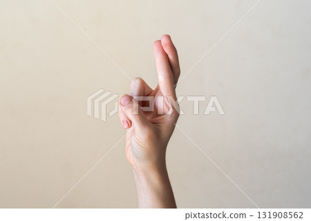 A close-up of a human hand with fingers crossed, symbolizing hope or a wish. The hand is light-skinned with neatly manicured nails against a neutral background. A close-up of a human hand with fingers crossed, symbolizing hope or a wish. The hand is light-skinned with neatly manicured nails against a neutral background. 131908562