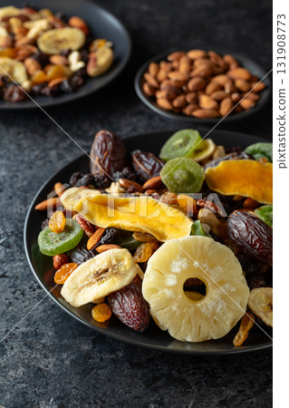 Dried tropical fruits, nuts, and raisins in black plate. 131908773