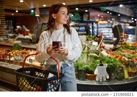 A woman is shopping in a grocery store while looking at her phone A woman is shopping in a grocery store while looking at her phone 131908821