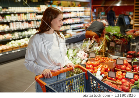 A woman is diligently pushing a shopping cart through a grocery store A woman is diligently pushing a shopping cart through a grocery store 131908826
