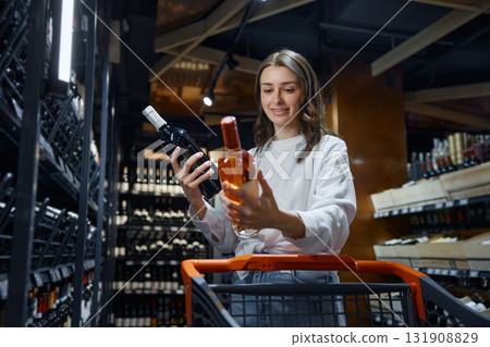 A woman is holding a bottle of wine inside a grocery store A woman is holding a bottle of wine inside a grocery store 131908829