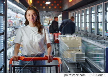 A woman is pushing a shopping cart in a supermarket aisle A woman is pushing a shopping cart in a supermarket aisle 131908843