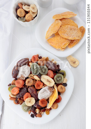 Mix of dried tropical fruits, nuts, and raisins on a white table. Mix of dried tropical fruits, nuts, and raisins on a white table. 131908844