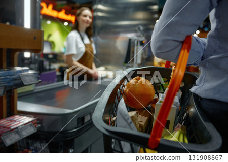 Closeup of man carrying a shopping basket full of groceries to the checkout in a store 131908867