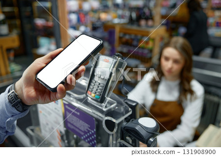 An individual is holding a mobile cell phone in front of a cash register 131908900