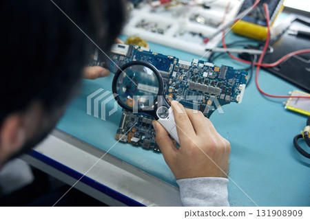 A person intently examining a detailed motherboard using a magnifying glass 131908909