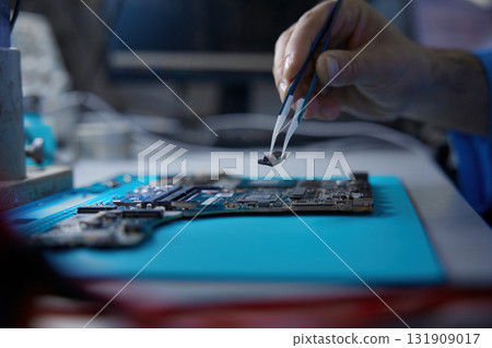 A technician works on a complex circuit board with precision tools and techniques A technician works on a complex circuit board with precision tools and techniques 131909017