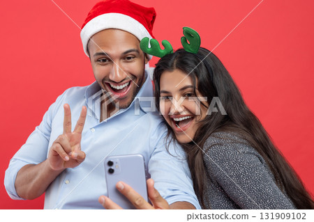 Happy man and woman taking selfie during Christmas celebration using smartphone for festive photo Happy man and woman taking selfie during Christmas celebration using smartphone for festive photo 131909102