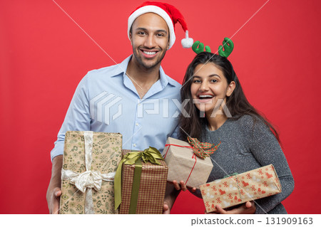 Cheerful couple holding gift boxes during Xmas celebration with festive hats and tinsel Cheerful couple holding gift boxes during Xmas celebration with festive hats and tinsel 131909163
