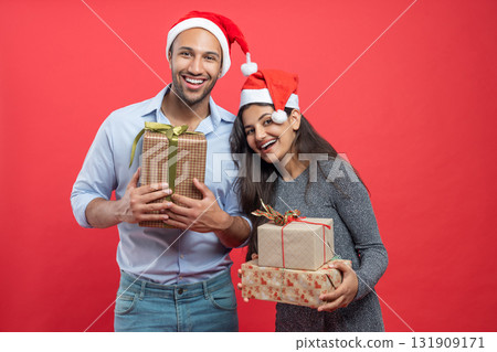 Cheerful couple holding gift boxes during Xmas celebration with festive hats and tinsel Cheerful couple holding gift boxes during Xmas celebration with festive hats and tinsel 131909171