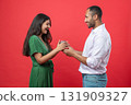 Cheerful couple celebrating birthday together on red background man presenting gift box to woman 131909327