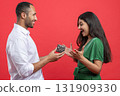 Cheerful couple celebrating birthday together on red background man presenting gift box to woman 131909330