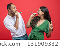 Happy couple celebrating holiday on party blowing in whistle isolated over red background 131909332