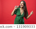 Playful woman enjoying her Christmas celebration indoors with joyful expression blowing noisemaker 131909333