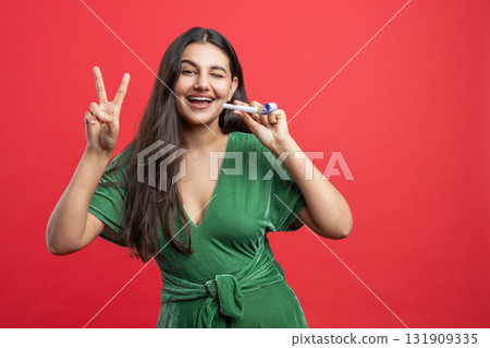 Festive beautiful woman winking showing v-sign and holding colorful tube while celebrating Festive beautiful woman winking showing v-sign and holding colorful tube while celebrating 131909335
