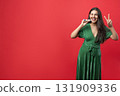 Playful woman enjoying her Christmas celebration indoors blowing noisemaker showing v-sign 131909336