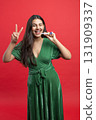 Beautiful woman celebrating her Christmas winking and showing victory sign holding noisemaker 131909337