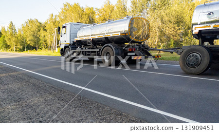 White milk tanker with drives along a highway through a forest landscape in summer. Delivery of milk from farms to the dairy plant. 131909451