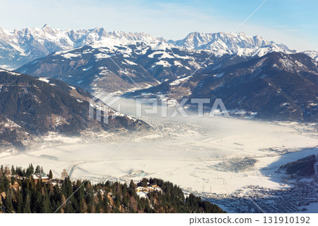 Scenic panoramic view snow-covered valley Kaprun Zell am See lies between majestic alpine peaks clear blue sky. Morning mist drifts frozen fields, creating serene winter panorama pure mountain beauty Scenic panoramic view snow-covered valley Kaprun Zell am See lies between majestic alpine peaks clear blue sky. Morning mist drifts frozen fields, creating serene winter panorama pure mountain beauty 131910192