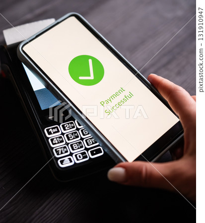 Girl Paying With A Smartphone Over A Wireless Terminal With Payment Approved Status On A Screen On A Table, Your Payment Was Approved 131910947