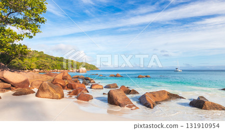 Sunlit tropical beach scene with smooth white sand, warm rocks and turquoise sea 131910954