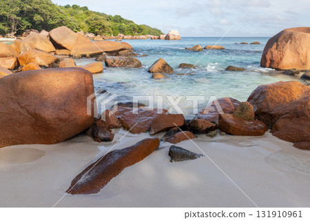 A serene coastal scene featuring large reddish boulders on a sandy beach, Seychelles A serene coastal scene featuring large reddish boulders on a sandy beach, Seychelles 131910961