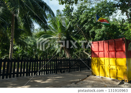Palm trees, a dark wooden fence, and a bright red-yellow shipping container 131910963