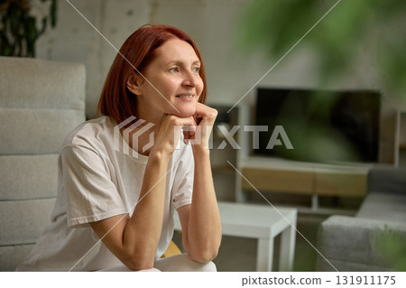 Thoughtful woman with red hair looking away while sitting comfortably at home Thoughtful woman with red hair looking away while sitting comfortably at home 131911175