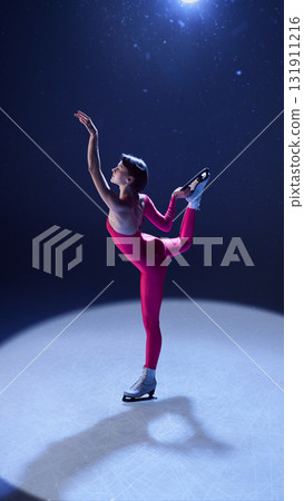 Elegant female skater in pink costume balancing in arabesque under spotlight on ice 131911216