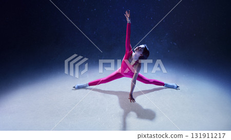 Female figure skater in pink bodysuit performing split stretch on ice with emotional precision Female figure skater in pink bodysuit performing split stretch on ice with emotional precision 131911217