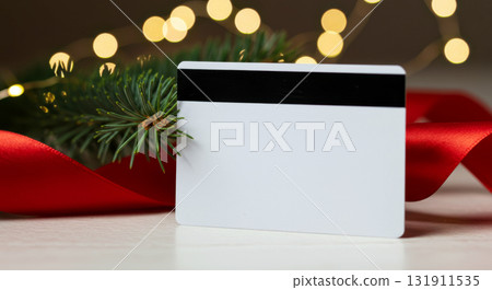 Blank white credit card on a table with red ribbon, fir branch, and festive bokeh lights. Holiday shopping concept. Blank white credit card on a table with red ribbon, fir branch, and festive bokeh lights. Holiday shopping concept. 131911535